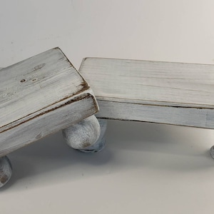 May include: Two white wooden tiered stands with rounded legs. The stands are made of distressed wood and have a whitewashed finish.