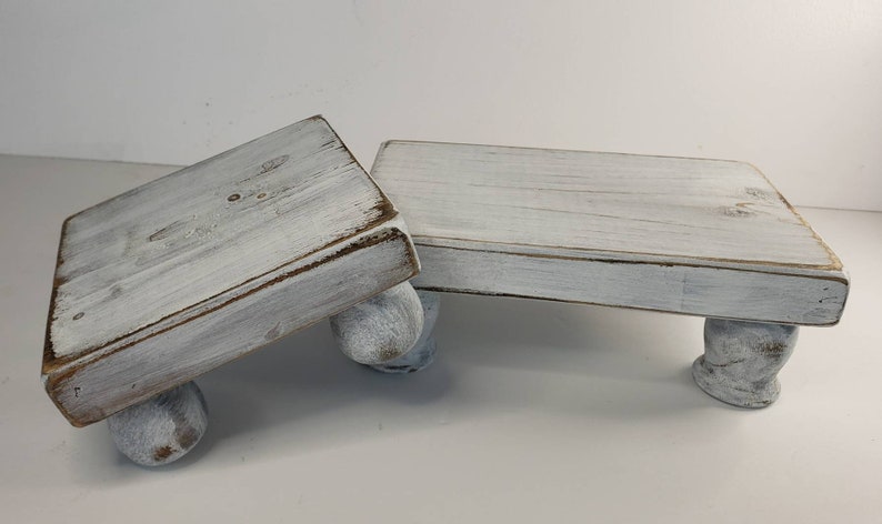 May include: Two white wooden tiered stands with rounded legs. The stands are made of distressed wood and have a whitewashed finish.