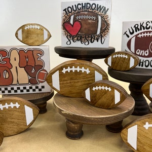 May include: A collection of wooden football-themed decorations, including signs that say "Game Day", "Touchdown Season", and "Turkey and Hoot", with a brown and white football on each sign.