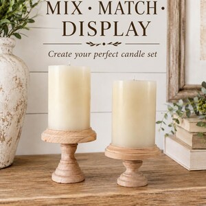 May include: Two ivory pillar candles on light wood pedestals. The candles are cylindrical and unscented. The pedestals have a turned design. The text "MIX &bull; MATCH &bull; DISPLAY" and "Create your perfect candle set" are visible.