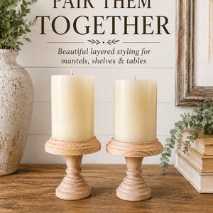 May include: Two ivory pillar candles sit atop light wood candle holders. The holders have a decorative, turned design. The image includes the text "PAIR THEM TOGETHER" and "Beautiful layered styling for mantels, shelves & tables."