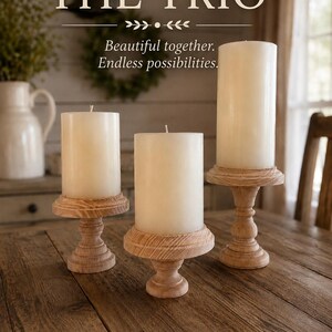 May include: Three ivory pillar candles on wooden pedestals. The candles are of varying heights and are displayed on a rustic wooden table. The text "THE TRIO" is at the top of the image, with the text "Beautiful together. Endless possibilities." below.
