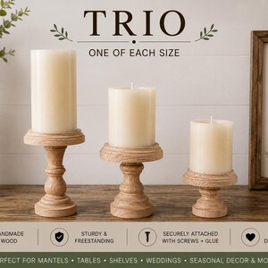 May include: A trio of wooden candle holders, each supporting a cream-colored pillar candle. The holders are in varying sizes and feature a turned design. The image includes the text "TRIO" and "ONE OF EACH SIZE".