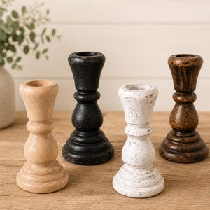 Peut inclure: Quatre bougeoirs en bois de diff&eacute;rentes couleurs : naturel, noir, blanc et marron. Chaque bougeoir a un design tourn&eacute; classique avec une base large et une coupe pour une bougie. Les bougeoirs sont dispos&eacute;s sur une surface en bois.