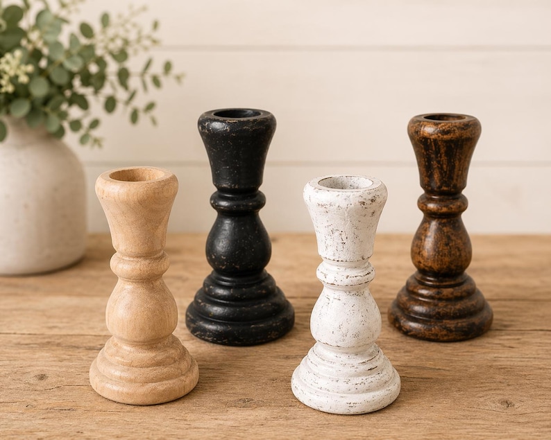 Peut inclure: Quatre bougeoirs en bois de diff&eacute;rentes couleurs : naturel, noir, blanc et marron. Chaque bougeoir a un design tourn&eacute; classique avec une base large et une coupe pour une bougie. Les bougeoirs sont dispos&eacute;s sur une surface en bois.