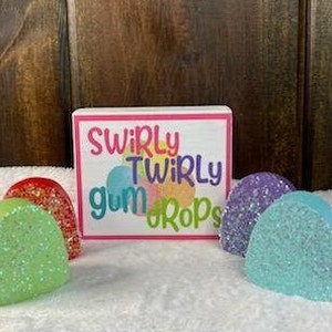 May include: Six colorful, glittery, half-circle shaped decorations with the text "Swirly Twirly Gum Drops" on a white sign.