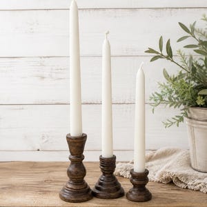 Peut inclure: Ensemble de trois bougies coniques blanches dans des bougeoirs en bois brun fonc&eacute;. Les bougeoirs ont un design tourn&eacute; d&eacute;coratif. Le texte "SET OF 3" est visible. Les bougies sont sur une table en bois.