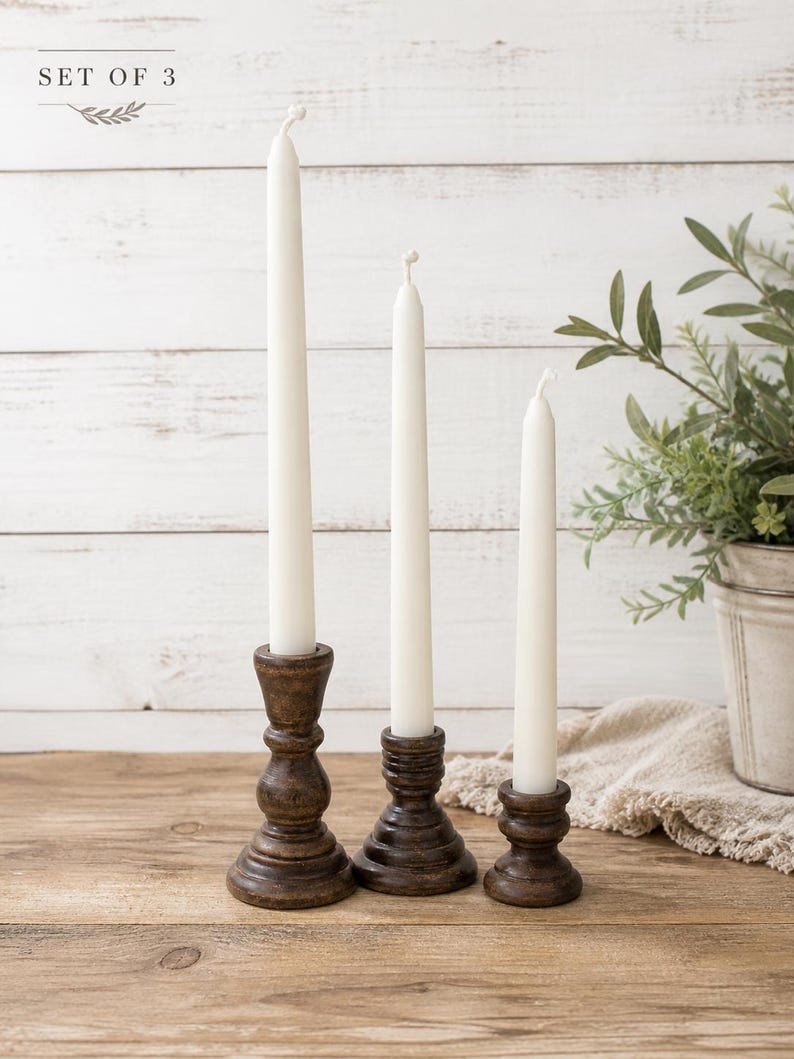 Peut inclure: Ensemble de trois bougies coniques blanches dans des bougeoirs en bois brun fonc&eacute;. Les bougeoirs ont un design tourn&eacute; d&eacute;coratif. Le texte "SET OF 3" est visible. Les bougies sont sur une table en bois.