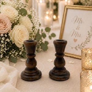 Peut inclure: Deux bougeoirs en bois brun fonc&eacute; de conception classique. Les bougeoirs sont pos&eacute;s sur une surface cr&egrave;me, avec un arrangement floral et des bougies en arri&egrave;re-plan. Une pancarte encadr&eacute;e indique "Mr. & Mrs."