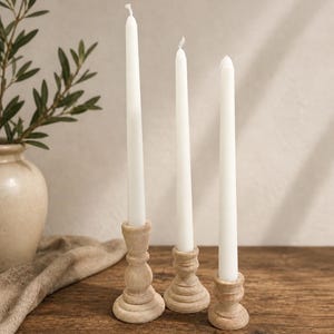 Peut inclure: Trois bougies blanches effil&eacute;es dans des bougeoirs d&eacute;coratifs en bois. Les bougeoirs sont de couleur marron clair et pr&eacute;sentent un motif sculpt&eacute;. Les bougies sont &eacute;teintes et reposent sur une surface en bois rustique.