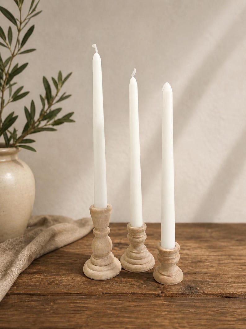 Peut inclure: Trois bougies blanches effil&eacute;es dans des bougeoirs d&eacute;coratifs en bois. Les bougeoirs sont de couleur marron clair et pr&eacute;sentent un motif sculpt&eacute;. Les bougies sont &eacute;teintes et reposent sur une surface en bois rustique.