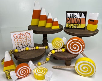 May include: Wooden tiered trays decorated with candy corn and candy themed decorations. The top tier has a sign that says "Official Candy Inspector". The middle tier has a sign that says "Trick Trick Trick or Treat". The bottom tier has a wooden candy corn.