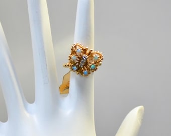 May include: A gold-toned ring with a butterfly design, adorned with opals and a small diamond cluster. The ring is set on a white hand, showcasing its intricate details and craftsmanship. The ring's design features delicate curves and textures.
