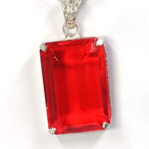 Op de afbeelding: Een zilveren hangerketting met een grote, rechthoekige, helderrode edelsteen. De edelsteen is gezet in een zilveren montuur en hangt aan een fijne zilveren ketting. De hanger heeft een klassiek, elegant ontwerp.