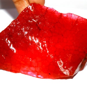 May include: A large, irregular, translucent red stone with a glossy, polished surface. The interior of the stone displays a distinct network of fine, web-like cracks or fractures that create a textured, vein-like pattern throughout the vibrant red material.