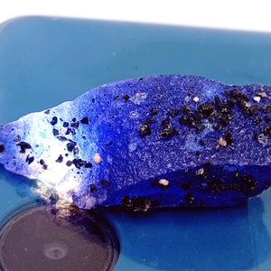 May include: A close-up of a blue, irregularly shaped rock with black and white flecks. The rock is sitting on a blue surface.