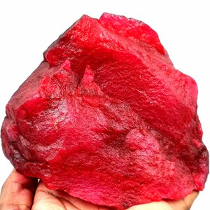 Könnte beinhalten: Ein großer, roher, roter Rubin-Edelstein. Der Rubin hat eine tiefe, satte rote Farbe und eine natürliche, unpolierte Oberfläche.