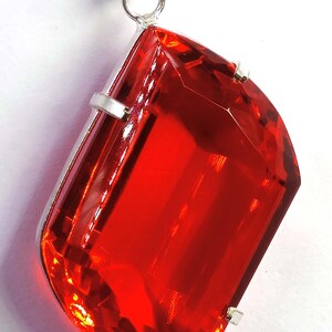 May include: A vibrant red gemstone pendant with a silver chain. The large, faceted gemstone is a striking shade of red, set in a silver bezel. The pendant hangs from a delicate silver chain, creating a bold and elegant jewelry piece.