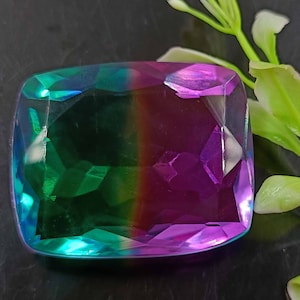 May include: A large, faceted gemstone with a green and purple color gradient. The gemstone is cut in a rectangular shape with rounded corners.