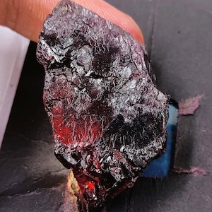 May include: A large, dark red and black gemstone with a rough, textured surface. The gemstone has a deep, rich color and is likely a variety of garnet.