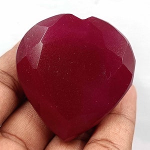 May include: A deep red heart-shaped gemstone with a faceted cut. The gemstone is polished and has a smooth, glossy finish.