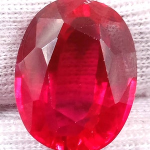 May include: A large, oval-shaped, faceted ruby gemstone with a deep red color.