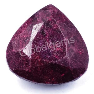 May include: A deep red ruby gemstone with a faceted, teardrop shape. The gemstone has a rich, dark red colour and a slightly textured surface.