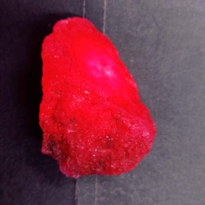 Peut inclure: Une grosse pierre précieuse rouge brute avec une surface cristalline brillante.