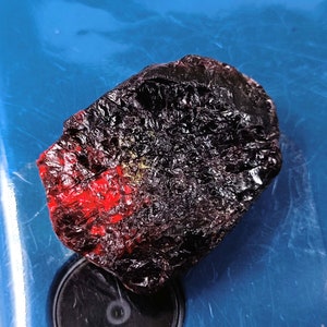 May include: A dark, rough, irregularly shaped rock with a red and black color pattern. The rock has a textured surface and appears to be a natural stone.