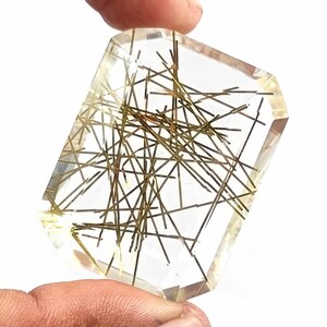 May include: A clear, faceted gemstone with gold and brown inclusions. The gemstone is cut in a rectangular shape.