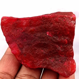 May include: A large, rough, red gemstone with a deep, rich colour. The gemstone has a natural, unpolished finish.