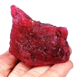 May include: A large, rough, red ruby gemstone. The ruby is a deep red color and has a natural, unpolished finish.