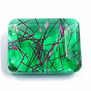 May include: A green gemstone with a faceted cut and a unique pattern of thin, dark lines. The gemstone has a translucent appearance and a slight shimmer.