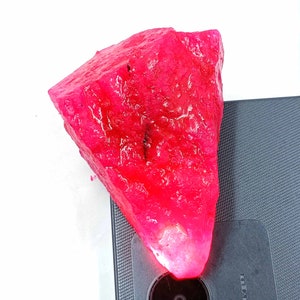 Puede incluir: Una gran gema de rubí rosa en bruto. El rubí está sobre una superficie negra.