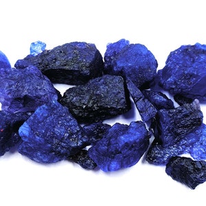 May include: A collection of blue crystal stones, some with a darker blue hue, scattered on a white background.