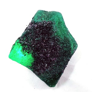 May include: A green and black gemstone with a rough, textured surface. The gemstone has a dark green color on one side and a lighter green color on the other side.
