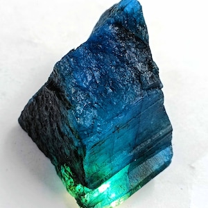 Op de afbeelding: Een groot, ruw, blauwgroen kristal met een donkerblauwe tot zwarte buitenkant en een lichter groene binnenkant. Het kristal heeft een gelaagde, gestreepte uitstraling.