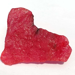 May include: A heart-shaped, pink, translucent gemstone with a rough, natural texture.