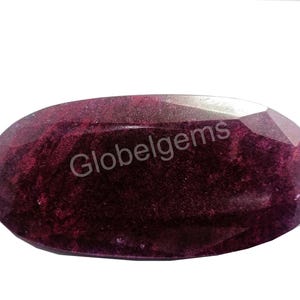 May include: A deep red oval gemstone with a smooth, polished surface. The stone has a subtle sparkle and a slightly cloudy appearance.  Globelgems is printed on the stone.