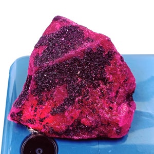May include: A large, rough, pink and black ruby crystal. The crystal has a deep, rich color and is covered in small, black inclusions.