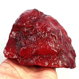 May include: A large, raw, deep red mineral specimen with a jagged, crystalline, and uneven surface texture. The stone displays varying shades of intense crimson and ruby red throughout its irregular, multifaceted, and naturally formed structure.