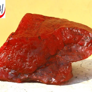 May include: A large, irregularly shaped, red gemstone. The gemstone has a smooth, polished surface and is translucent.