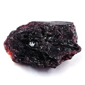 May include: A large, dark purple, rough-cut gemstone with a deep, rich color. The gemstone has a natural, unpolished surface and is a beautiful example of raw crystal.