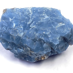 May include: A raw, unpolished chunk of blue opal mineral with a vitreous, glass-like luster. The stone features an irregular, jagged shape with deep cerulean and sky-blue color variations across its fractured, translucent surface texture.