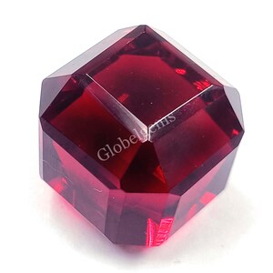 May include: A deep red gemstone with a faceted, square shape. The gemstone is cut into a cube with many facets.