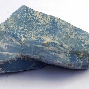 May include: A rough-hewn, irregularly shaped, blue-gray stone with a textured surface. The stone has areas of lighter, almost white, coloration. The overall appearance suggests a natural mineral or gemstone, possibly a raw crystal.
