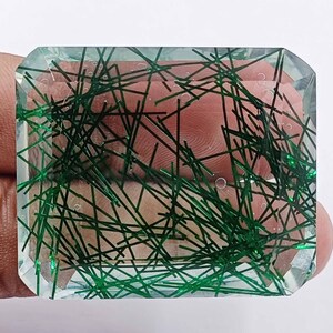 May include: A clear, faceted gemstone with green inclusions. The gemstone has a rectangular shape and is cut into a emerald shape.