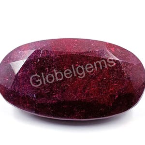 May include: A deep red oval gemstone with a faceted cut. The gemstone has a rough, natural texture.