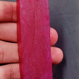 Peut inclure: Une grosse pierre précieuse de rubis rectangulaire rouge foncé. Le rubis est lisse et poli, avec un léger éclat.