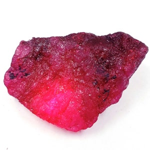 Puede incluir: Una gran gema de rubí rosa en bruto con un tono rojo intenso. La gema tiene un aspecto natural y sin pulir.